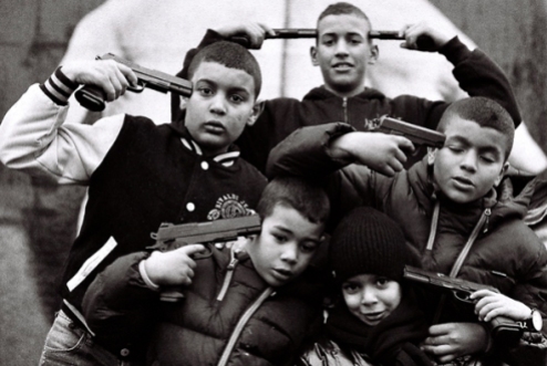 Enfants jouant avec des armes factices, simulant le suicide collectif, devant l'oeuvre de Bandian.